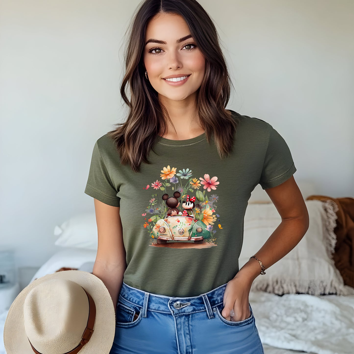 A women wearing olive-colored unisex t-shirt featuring an illustration of Mickey and Minnie Mouse with flowers and a vehicle.