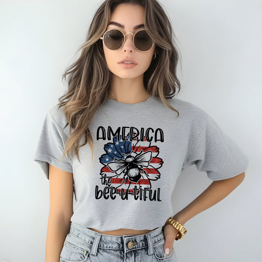 Woman wearing a gray t-shirt with 'America the bee-u-tiful' design with sunflower with american flag graphic with bee